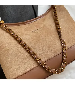Close-up of brown suede shoulder bag with gold chain strap and brand logo detail