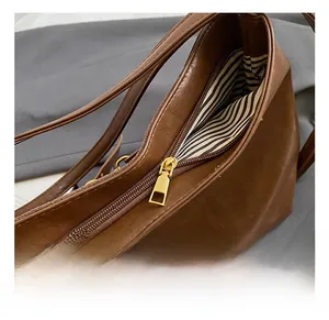 Detail view of the brown leather tote bag showing gold zipper and striped inner lining