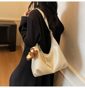 Détail d'un sac cabas blanc crème avec pendentif ours sur l'épaule d'un mannequin