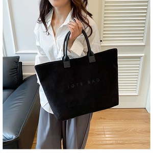 Close-up of black corduroy tote bag featuring embossed logo and durable handles
