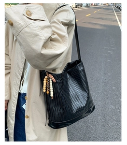 Détail du sac seau noir tressé avec pendentif en perles de bois et bandoulière