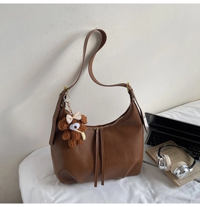Détail du sac demi-lune en similicuir marron avec breloque peluche sur un lit blanc