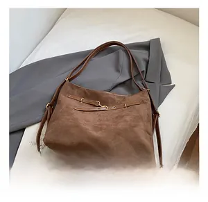 Close-up of brown suede tote bag with leather strap detail and metallic buckle