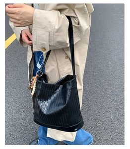 Gros plan d'un sac seau tressé noir avec bijou de sac perlé porté par un mannequin
