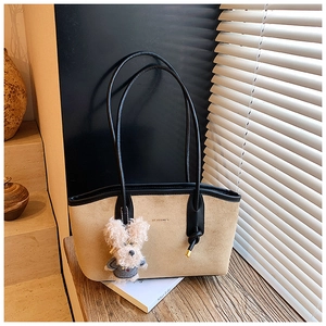 Detail of soft suede tote bag with black piping, knot strap, and plush puppy charm