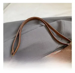 Detail of brown suede shoulder bag showing double thin straps and golden metal buckles