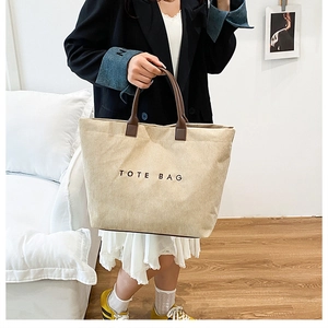 Spacious corduroy tote bag in cream white with brown handles shown in a home setting