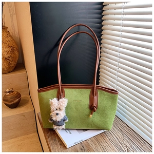 Detail of green suede tote bag with brown leather straps and cute dog charm on desk