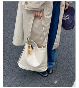 Détail du tissage du sac cabas crème avec breloque en perles de bois sur fond asphalte