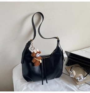 Détail du sac hobo noir avec breloque ours et casque argenté sur un bureau blanc