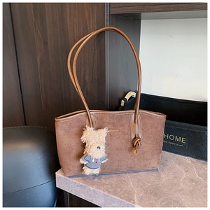 Detail of brown suede tote bag with slim straps, knot hardware and plush dog charm