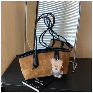 Detail of a brown suede tote bag with black leather straps and a plush dog charm