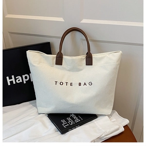 Close-up of minimalist corduroy tote bag with brown leather handles and printed text