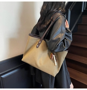Detail showing high-capacity khaki canvas tote bag with leather straps and beaded tassel