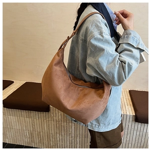 Side view of a large brown suede hobo bag with a zipper and wide shoulder strap