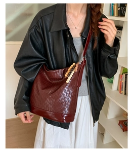 Détail d'un sac seau tissé bordeaux avec motif à damier et bandoulière perlée en bois