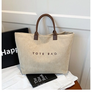 Detail of off-white corduroy tote bag featuring TOTE BAG embroidery and brown leather handle