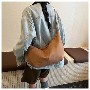 Detail view of large brown suede hobo bag worn on shoulder in a minimalist setting