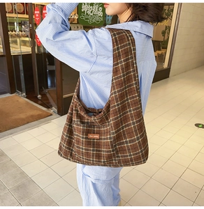 Detail of large brown plaid canvas tote bag with leather logo tag for daily commute