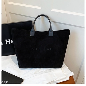 Detail of black corduroy tote bag with embossed text and leather handles on white background