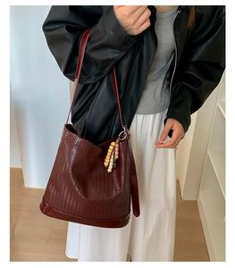 Détail du sac seau bordeaux en cuir tressé avec pompon en bois porté par un mannequin