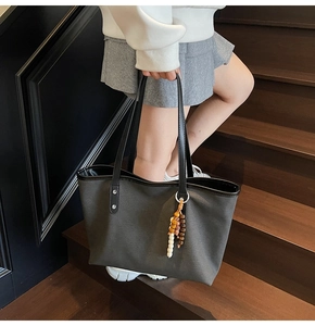 Detail view of large charcoal canvas tote bag with wooden bead charm and leather handles