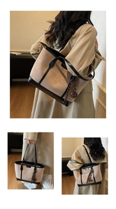 Detail view of a large tote bag featuring canvas texture, black leather trim, and woven charms