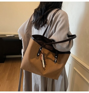 Detail of a large brown tote bag with leather trim and decorative beaded pendant charm