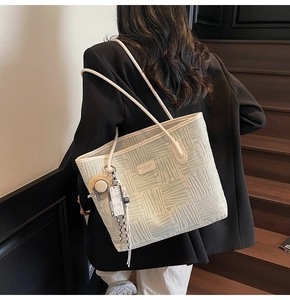 Detailed view of beige tote bag featuring geometric texture and decorative hanging pendant