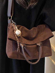 Brown suede tote bag with baseball charm worn by a model in a stylish indoor setting