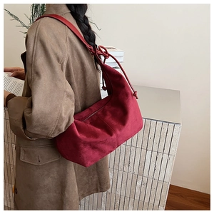 Detail of burgundy suede shoulder bag featuring a knotted strap and retro silhouette