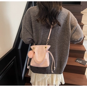 Detail view of pink drawstring bucket bag with gold chain and plush ball on a model