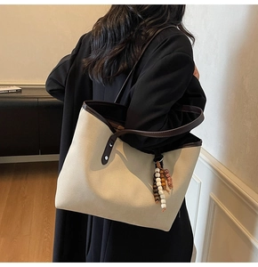 Detailed view of the large beige tote bag with brown trim and wooden bead tassel ornament