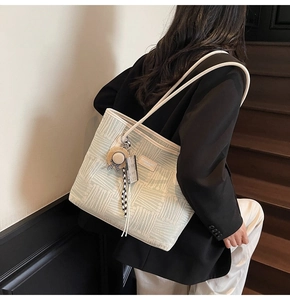 Detail of light green patterned tote bag with straw hat charm on model in office setting