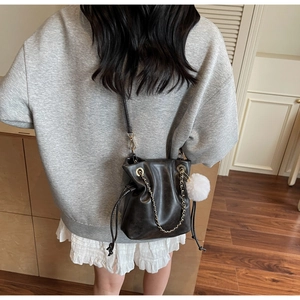 Detail of black drawstring bucket bag with gold chain and white fuzzy pompom charm