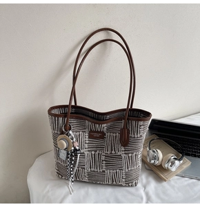 Close-up of woven tote bag with leather strap, logo patch and mini straw hat charm