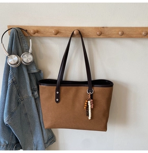 Detail of canvas tote bag with leather straps and decorative bead charm on a hook