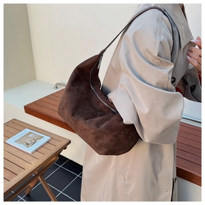Detailed view of deep brown suede hobo bag on model wearing a classic beige trench coat