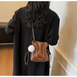 Close-up of caramel brown drawstring bucket bag with gold chain and white pompom charm