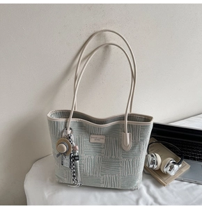 Detailed texture of light blue woven fabric tote bag with cream leather strap and charm