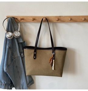 Detail of canvas tote bag with leather handles and beaded charm on wooden hook