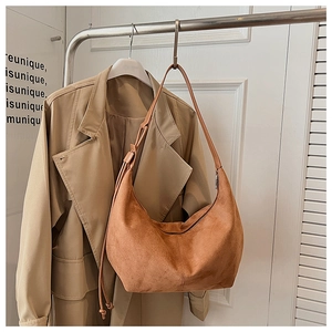 Detail of caramel suede hobo bag hanging with a trench coat showing soft texture and straps