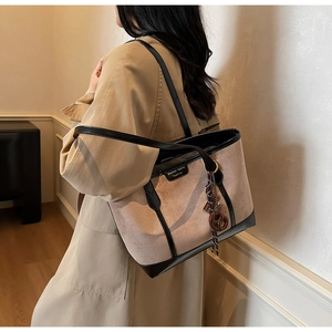 Detail of khaki suede tote bag with brown leather trim and hanging charm accessory