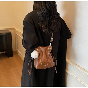 Detail view of a brown drawstring bucket bag with metal chain and white pompom charm
