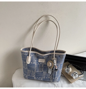 Detail view of woven blue and white tote bag with leather strap and mini straw hat accessory