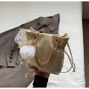 Detail of cream drawstring bucket bag with gold chain handle and plush ball charm