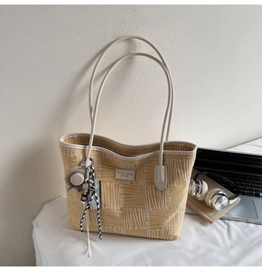 Detailed close-up of yellow woven tote bag with geometric texture and decorative charms