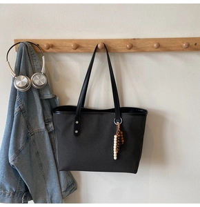 Detail of a minimalist black tote bag with colorful wooden bead charm and silver hardware