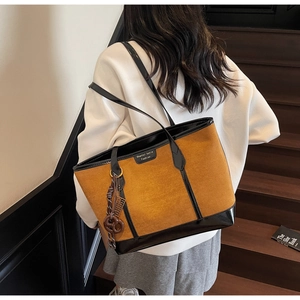 Brown suede tote bag with black patent leather trim shown on a model on stairs