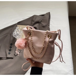 Detailed shot of pink drawstring bucket bag with gold chain handle and plush charm decor